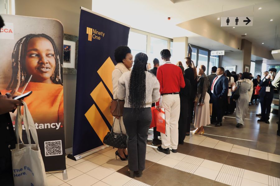 People line up for event registration by banners in a bright hallway.