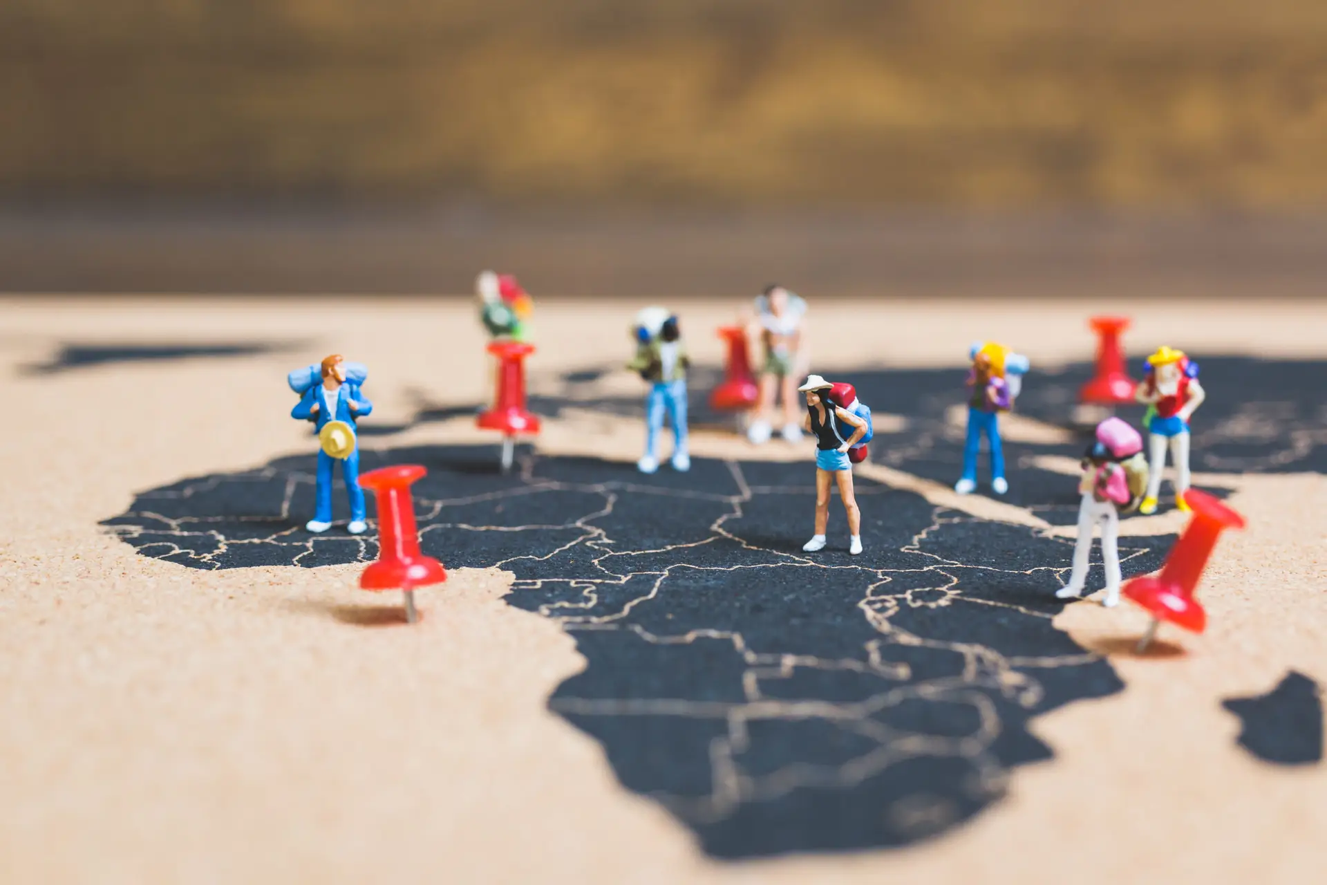 Miniature figures and red pins placed on a cracked dark map surface, resemble a travel scene.