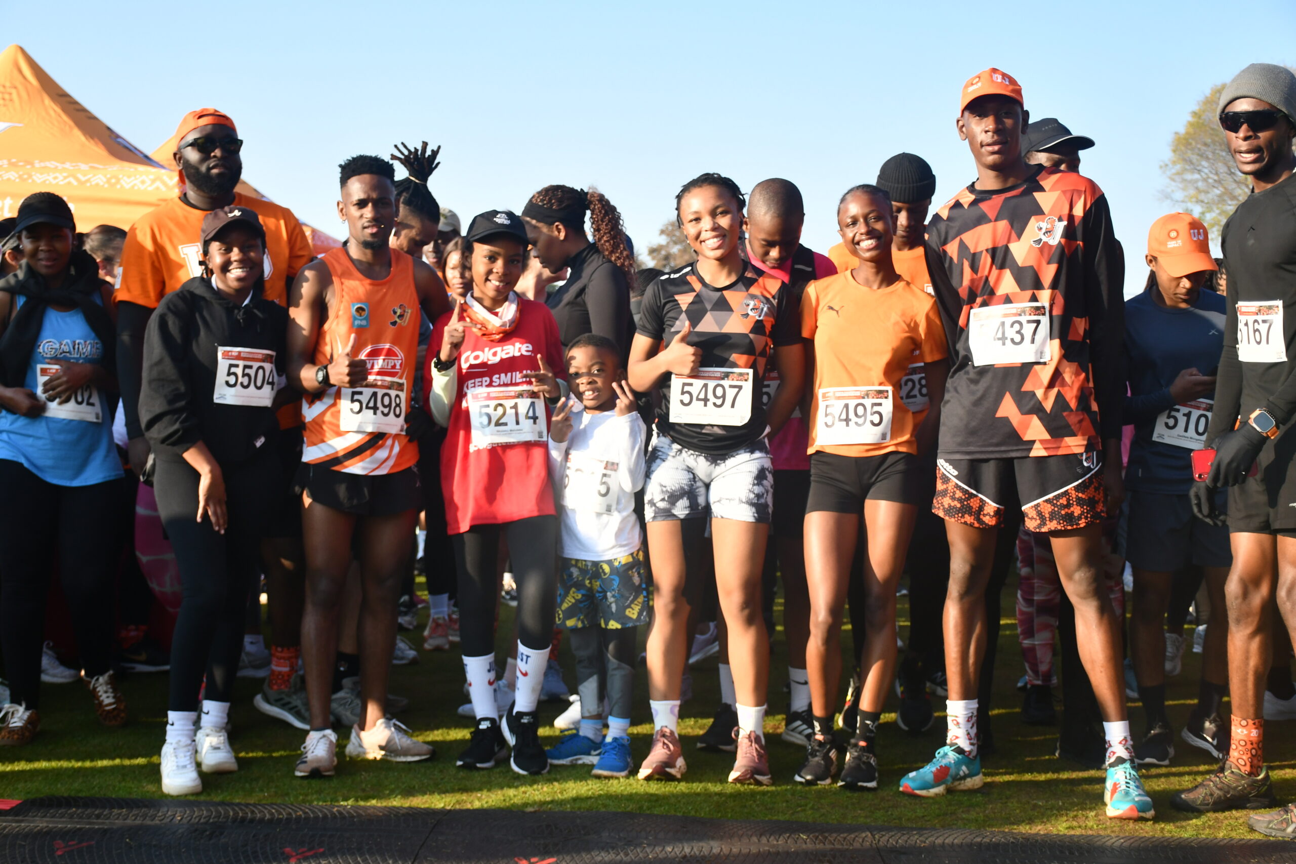 Group of runners at the race start on a sunny day, bib numbers visible on their shirts