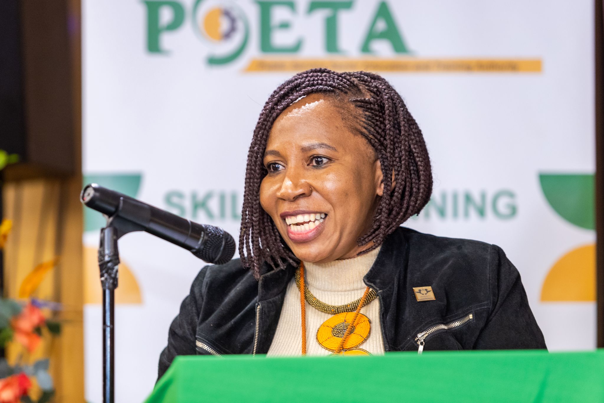 Smiling woman with braided hair speaking into a microphone at a podium during a presentation.